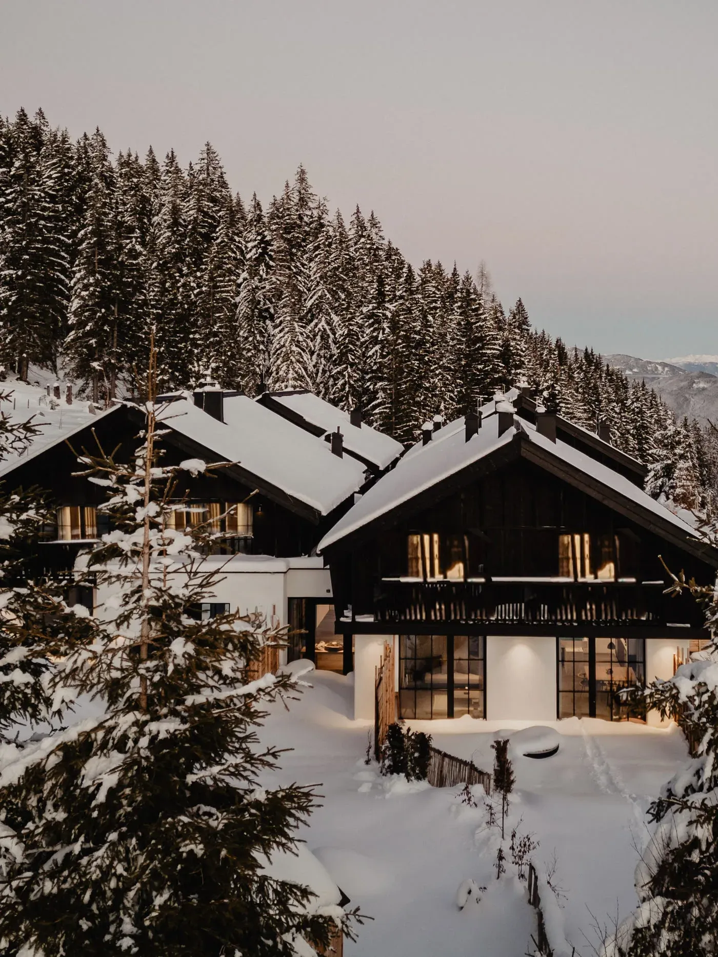 Birgkar-Lodge im Winter mit beleuchteter Fassade, verschneiten Bäumen und Blick ins Tal am Hochkönig