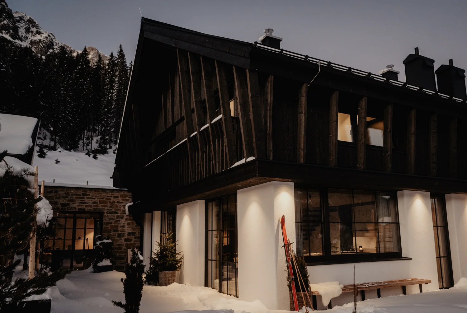 Beleuchtete Birgkar-Lodge in der Dämmerung – schwarze Holzfassade im Schnee